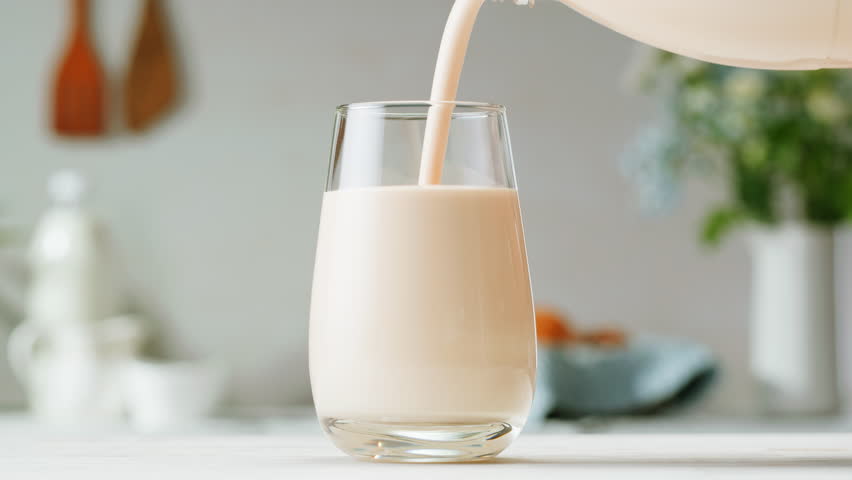 Pouring kefir yogurt into glass cup close-up. Glass with kefir or milk, lactic acid product dairy products concept. Drinking fresh lactose free in morning.
