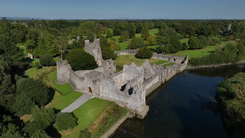 Desmond Castle, Adare, County Limerick, Ireland, September 2024. Drone orbits clockwise and pulls back rising above River Maigue with entrance through the broken walls of the historic Norman ruin.