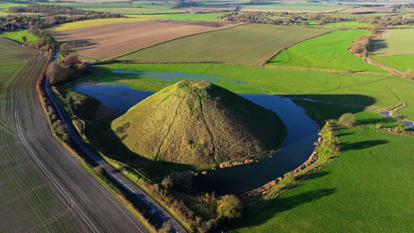 Aerial shot of Silbury Hill and countryside in low sun with long shadows