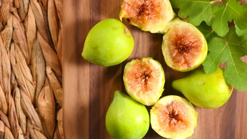 Fig fruits. Ripe sweet yellow, green figs fruit with leaves close up, rotating on wood background, top view 
