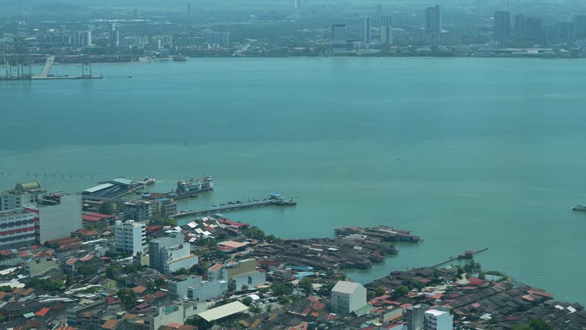 Waterfront views of Penang, Malaysia, featuring a ferry terminal with several boats docked and a ferry crossing the sea, time-lapse shot.