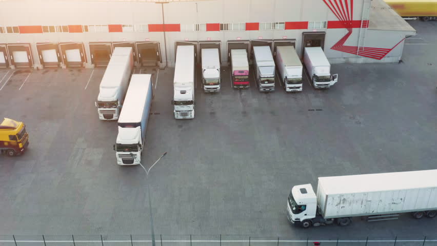 Aerial View of Logistics Distribution Center with Loading Docks and White Trucks at Sunset, Modern Terminal with Parked Semi Trailers 