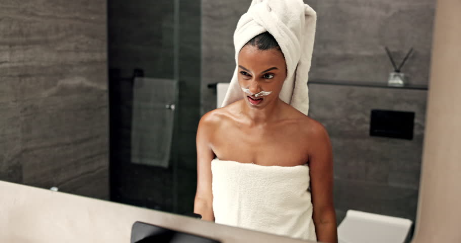 Woman, humor and lotion with mirror, funny face or fake mustache for comedy, silly or goofy expression in bathroom. Female person, masculine or confidence with facial wax cream, SPF or moisturizer