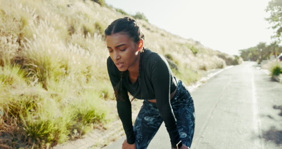Woman, runner and tired on road, nature and rest for fitness, training and breathe in countryside. Girl, outdoor and workout in sunshine for wellness with fatigue, exhausted or reflection in Colombia