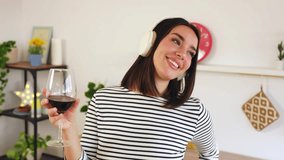 Happy pretty woman drinking red wine while enjoying online music with wireless headphones and singing in the kitchen at home - Powered by Shutterstock - Get 15% off with code: PIKWIZARD15