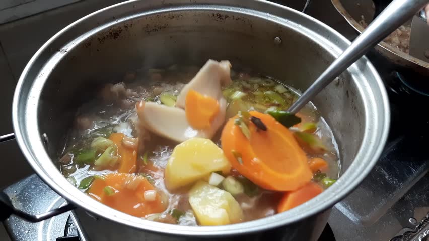 A pot of homemade meat soup with fresh vegetables, including carrots and green onions. A hearty and flavorful dish, perfect for comfort food and culinary themes