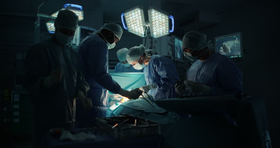 Diverse Surgical Team Working in a Darkened Operating Room Surrounded by Advanced Medical Equipment. Doctors Performing a Complex Surgery with the Help of Laparoscopic Equipment