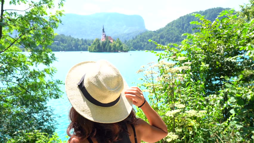 Woman wearing a straw hat enjoying the breathtaking view of bled castle on lake bled, slovenia, a popular tourist destination in the julian alps
