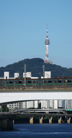 Subway train ride at Dangsan railway bridge over Han river, slow motion telephoto shot. Seoul TV tower visible on background. Fine vertical shot of daily commute of Korean capital city