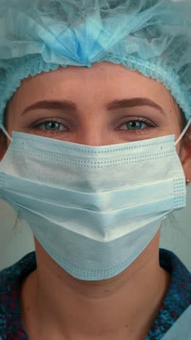 Portrait of smiling female doctor removing medical face mask, close up. Happy young woman takes off protective medical mask after quarantine. Pandemic protection. Vertical video