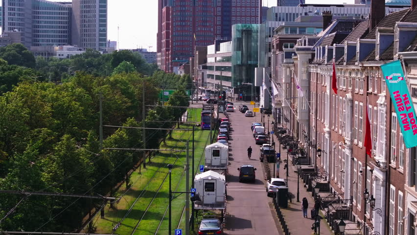 Aerial view of a lively street in The Hague with cars, historic buildings, and green urban spaces on a sunny day, showcasing European city life and architecture