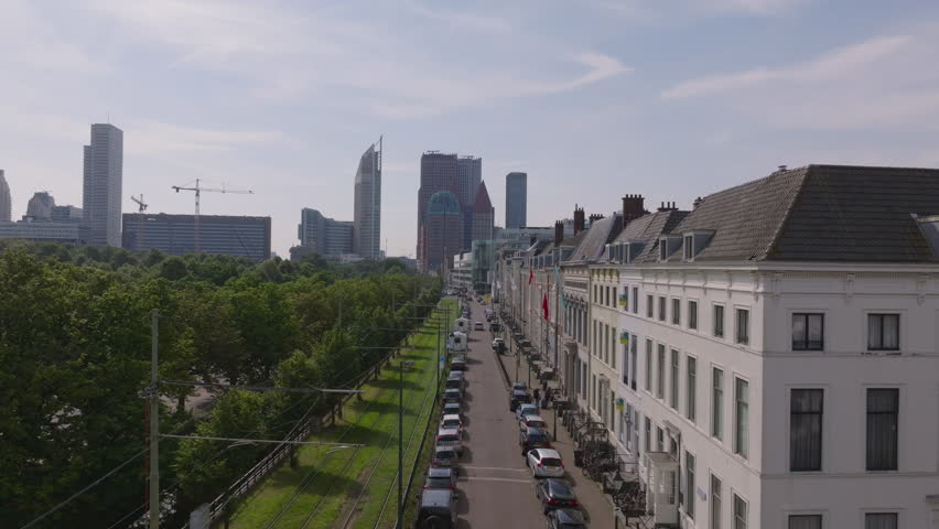 Tram and parked cars along a tree lined street in The Hague, with modern skyscrapers and charming buildings from an aerial perspective