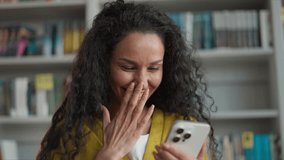 Excited Latina Caucasian Hispanic woman holding mobile phone smartphone smile amazement emotional exam results high school university library student female girl gadget social media delighted study - Powered by Shutterstock - Get 15% off with code: PIKWIZARD15