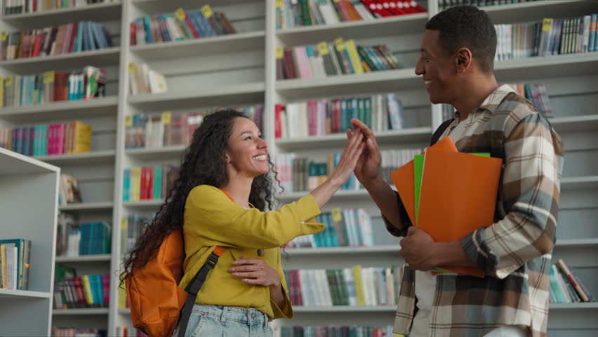 Latino Arabian woman backpack African American man approach say hello meet high five smile friends classmates students teenagers communication library girl educate guy holding books textbooks learners