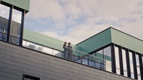 Business colleagues talking at balcony office building. Professional partners discussing work enjoying city view. Two corporate coworkers enjoy communication at outdoors meeting in front blue sky. - Powered by Shutterstock - Get 15% off with code: PIKWIZARD15