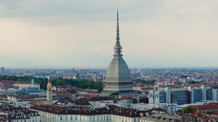 An aerial view of Turin bathed in the golden hues of sunset, with the Mole Antonelliana standing tall amidst a backdrop of the Alps.