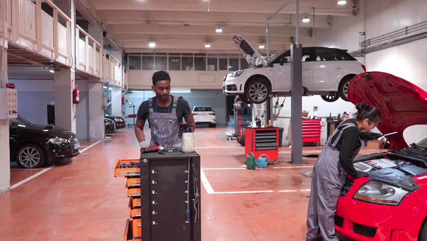 Mechanics organizing tools and repairing a red car in a professional auto repair shop, slow motion