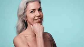 Portrait of a happy, confident mature woman with grey hair and a tattoo, smiling against a blue background, embodying beauty at every age. - Powered by Shutterstock - Get 15% off with code: PIKWIZARD15