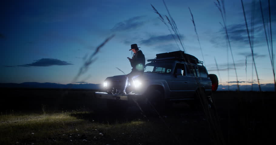 Young woman sitting in her car surrounded by nature at night, using her smartphone to photographing while embracing the peace and tranquility of the serene landscape
