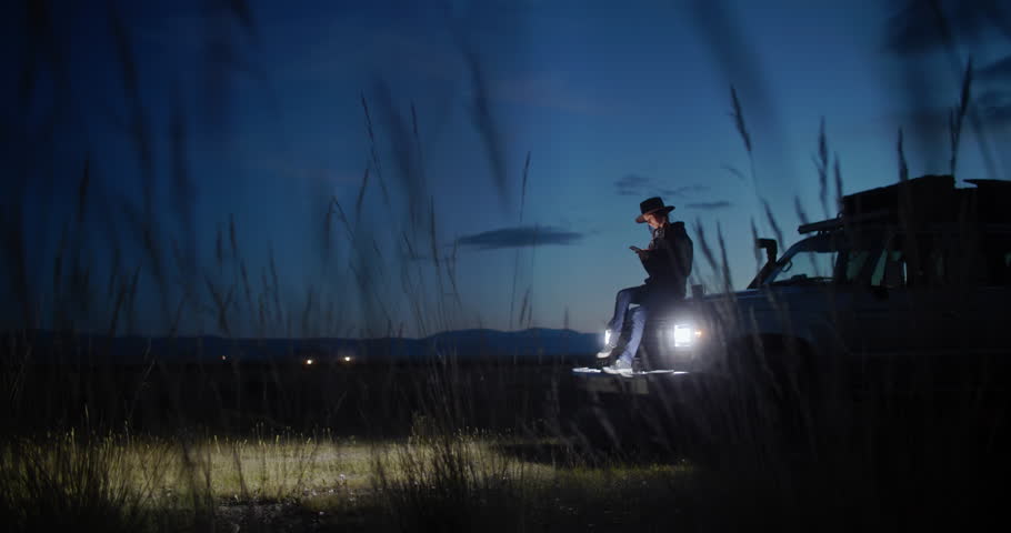 Young woman sitting in her car surrounded by nature at night, using her smartphone to photographing while embracing the peace and tranquility of the serene landscape