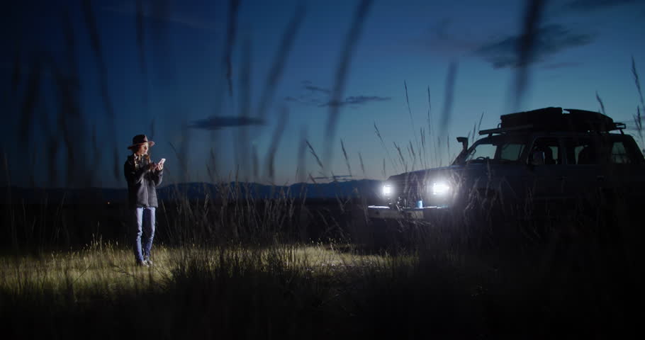Young woman sitting in her car surrounded by nature at night, using her smartphone to photographing while embracing the peace and tranquility of the serene landscape