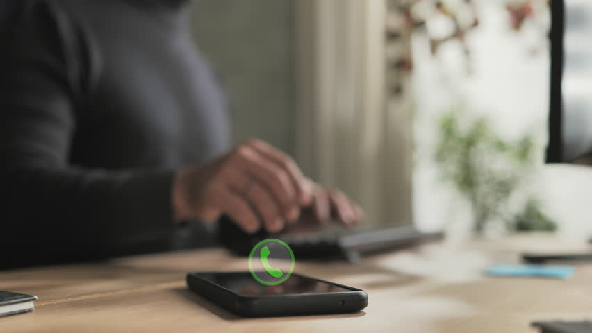 person at computer receiving phone call on smartphone mobile,male employee at the desk receives phonecall,icon symbol showing on the screen