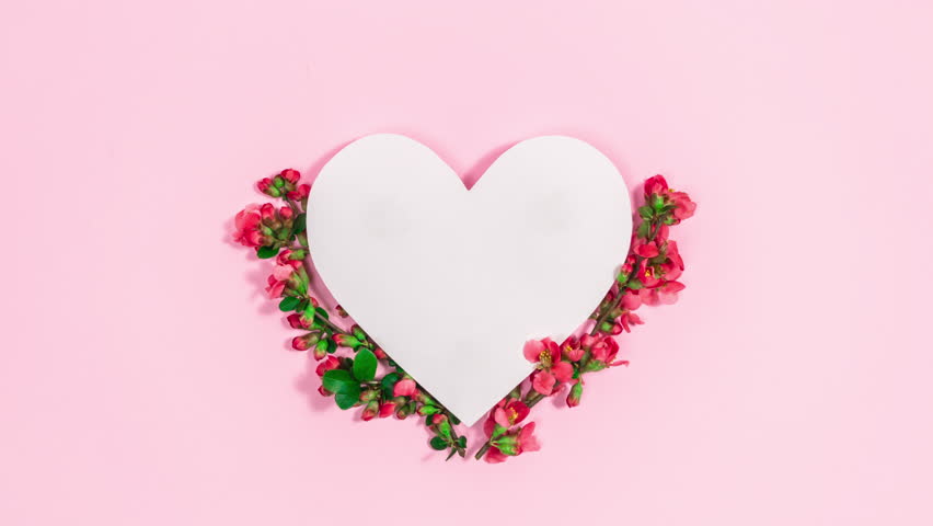 Natural branches with spring red buds and flowers appear near the white paper heart. Concept of the arrival of spring or greeting card for mother's, women's, birthday day. Copy space. Text template.