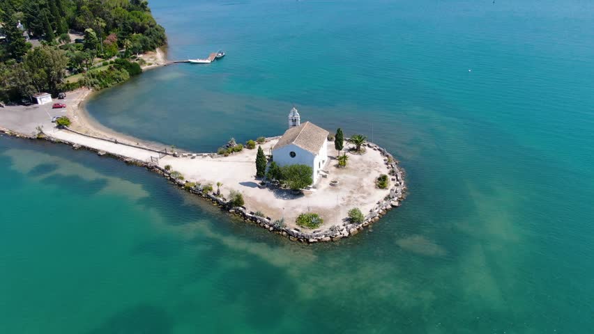 Picturesque coastal chapel on a small island, accessible by a stone path. Serene waters surround the tranquil scene.