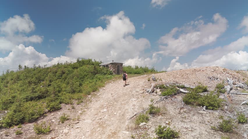 Girl walking on a mountain towards a little hut.