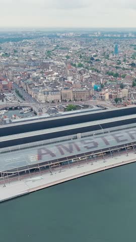 Vertical video. Amsterdam, Netherlands. Amsterdam Central Station. Amsterdam Centraal - The largest train station in the city, built in 1889. Bay IJ (Amsterdam), Aerial View, Point of interest