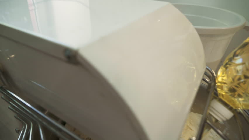 A Close-up of a Complex Automatic Kneading Machine that is mixing the dough. Adding the oil from the bottle to assist the dough mixing process. Slowly Mixing the dough for the Food Production.
