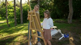 A young art teacher assisting a girl during a painting session on an easel in a tranquil park setting fostering creativity and learning - Powered by Shutterstock - Get 15% off with code: PIKWIZARD15