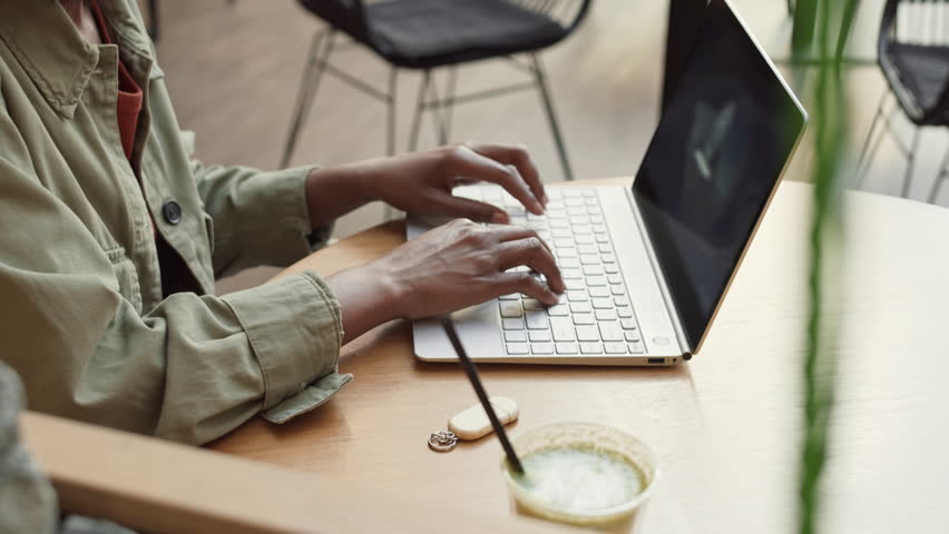 High angle view of unrecognizable African woman wearing casual clothes sitting at desk in modern office and inserting flash drive into computer