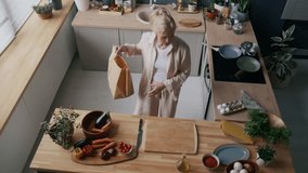 Top-down view of mature Caucasian woman organizing fresh vegetables and ingredients on wooden countertop in bright, plant-filled kitchen with modern appliances and warm ambiance - Powered by Shutterstock - Get 15% off with code: PIKWIZARD15