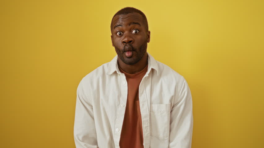 African american man wearing shirt standing in front of yellow background making a funny fish face expression with crazy and comical gesture using lips
