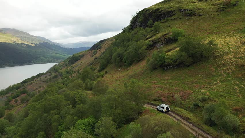 Aerial view of 4x4 on mountain dirt track above loch in picturesque valley, Scottish Highlands, Scotland.