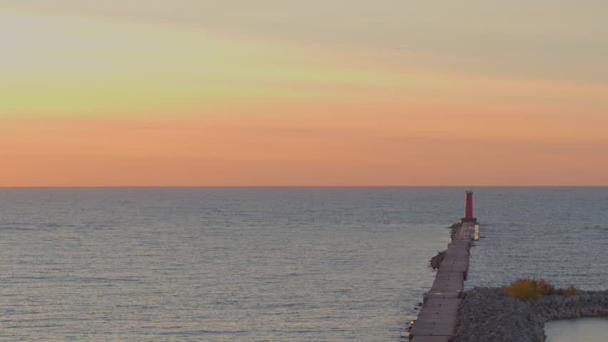 Aerial over Lake Michigan with push towards Sheboygan Lighthouse in Wisconsin at sunrise with a beautiful hombre sky and gentle relaxing waves