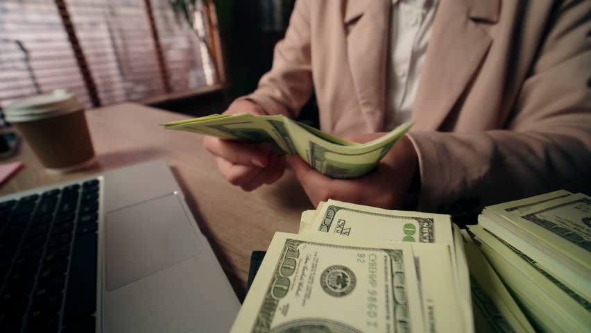 Close up rich Caucasian businesswoman female girl business woman office worker unknown boss leader sit desk laptop computer counting dollars money banknotes wealth salary profit finance jackpot indoor