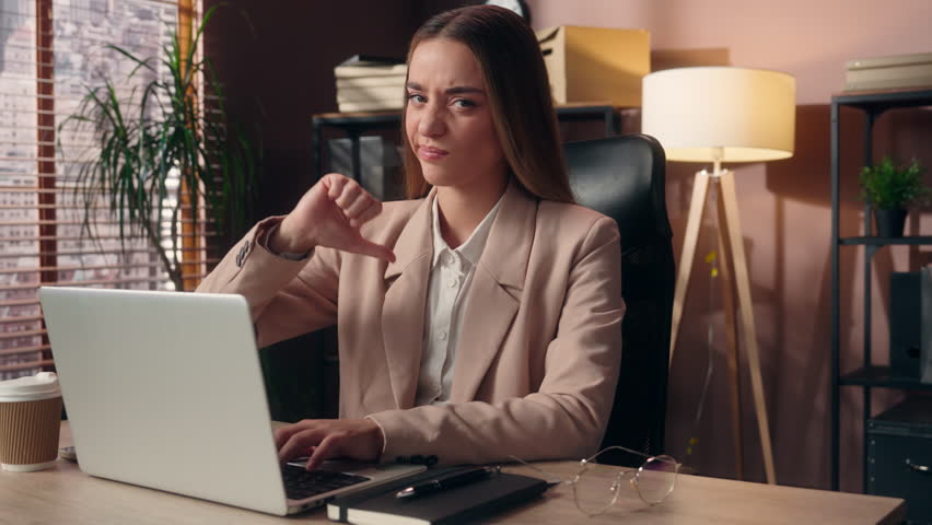 Unhappy disappointed Caucasian business woman girl female businesswoman entrepreneur worker working online laptop computer showing thumb down rejection finger dislike gesture negative reaction indoor