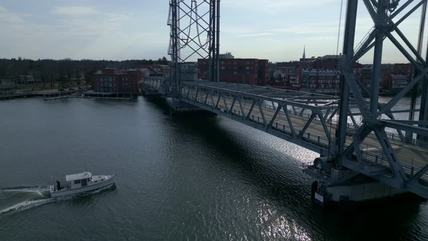 Aerial view of boat passing under vertical-lift World War I Memorial bridge in Portsmouth, unique design and flowing river, infrastructure and scenic city.