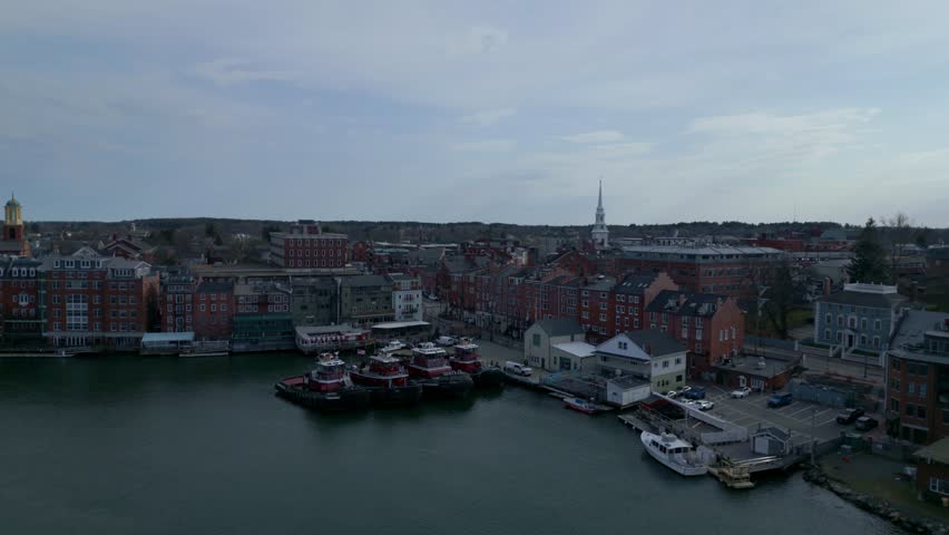 Portsmouth harbor aerial ascend pullback with docked tug boat ships, calm waters, and industrial activity along coastal port town