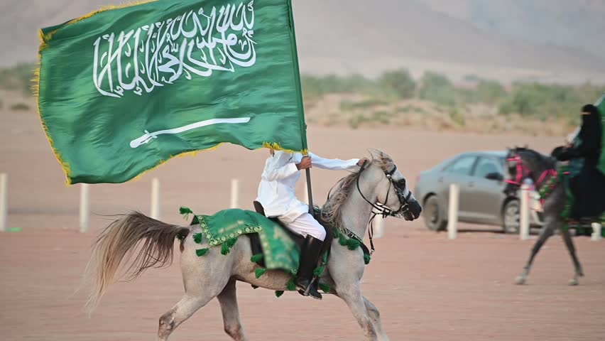 A Saudi man in traditional attire gallops on a majestic Arabian horse across the desert, proudly holding the Saudi flag. Celebrating Saudi national and founding day.