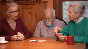 Family members gather around a wooden table playing cards and sharing laughter in a cozy living room. The elderly couple relishes quality time with their daughter. - Powered by Shutterstock - Get 15% off with code: PIKWIZARD15