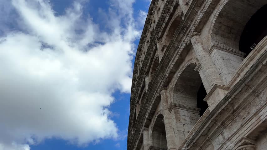 Colosseum in ancient Rome, Italy looking up into the blue cloudy sky while birds fly