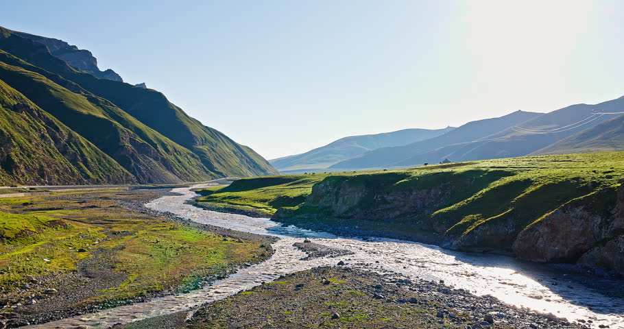 Flowing river and green grassland with mountain natural landscape in summer. Beautiful scenery along the Duku Highway in Xinjiang, China.