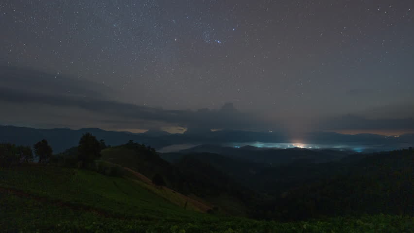 Timelapse of beautiful moonlight glowing with starry, clouds blowing over vegetable hill and mountain range in countryside at Chiang Dao, Chiang Mai, Thailand