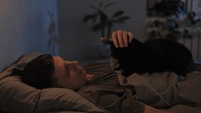 Cat lies on man reclining in bed. Lovely pets. Handsome young man resting lying in bed with his cat. Lovely pets. - Powered by Shutterstock - Get 15% off with code: PIKWIZARD15