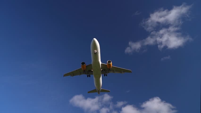 Low Angle View of Passenger Airplane with Yellow Engines Flying Across Blue Sky in Smooth Motion