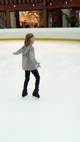 Little girl skates trains doing exercises, spin on indoor ice rink. Child figure skating. Childrens sport. Vertical shot