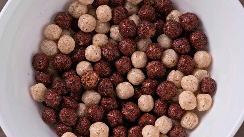 Milk pouring into chocolate cereal balls bowl in slow motion. Crispy cereal for breakfast. Close-up of Crispy cereal for breakfast.